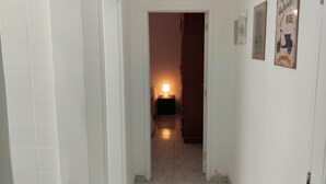 A narrow hallway with a tiled floor leading to a room with a bed and a nightstand with a lamp. - Leblon Apartment (Rio de Janeiro)