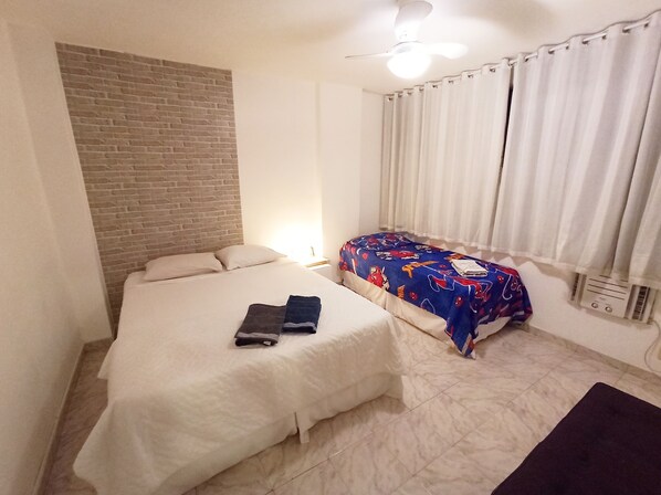 Una habitación con dos camas, una pared de ladrillo, un ventilador de techo y una ventana con cortinas.