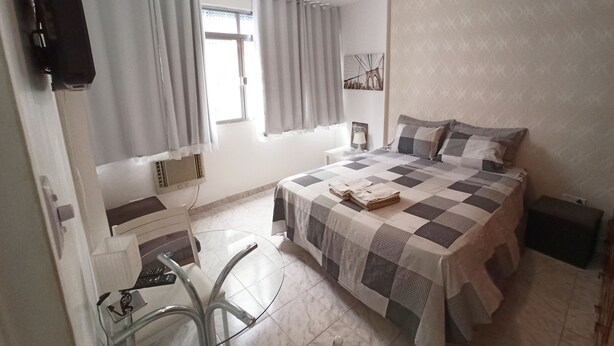A bedroom with a bed, a desk, and a chair. There is a window with curtains, a ceiling fan, and a wall-mounted TV. - Leblon Apartment (Rio de Janeiro)