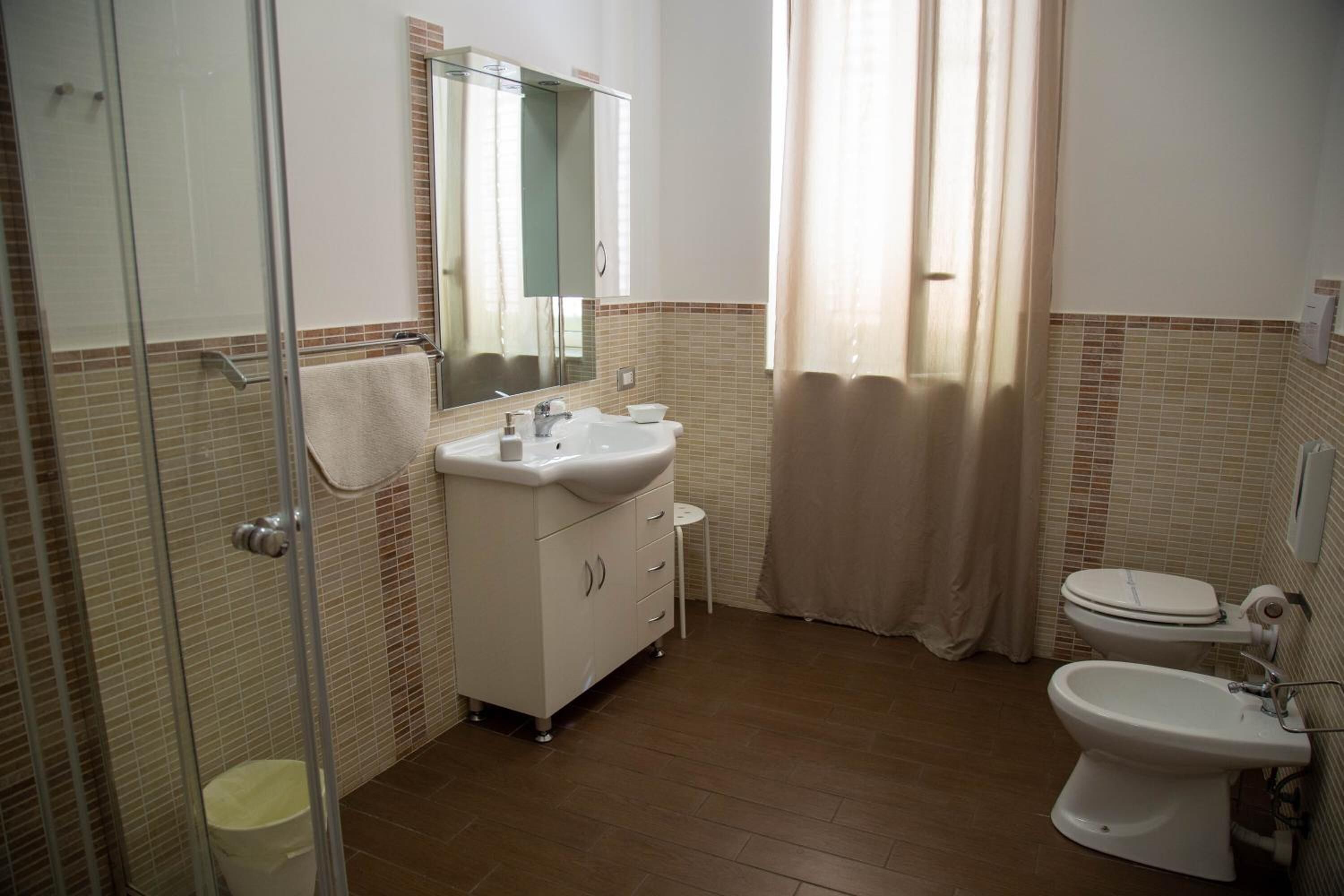 A bathroom with a glass shower enclosure, a sink with a mirror above it, a toilet, and a bidet.
