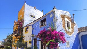 A colorful building with a blue facade, a yellow corner, and a pink flowering plant in the foreground. - B&B Del Centro (Partinico)