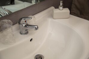 A white bathroom sink with a chrome faucet, a soap dispenser, and a drain.