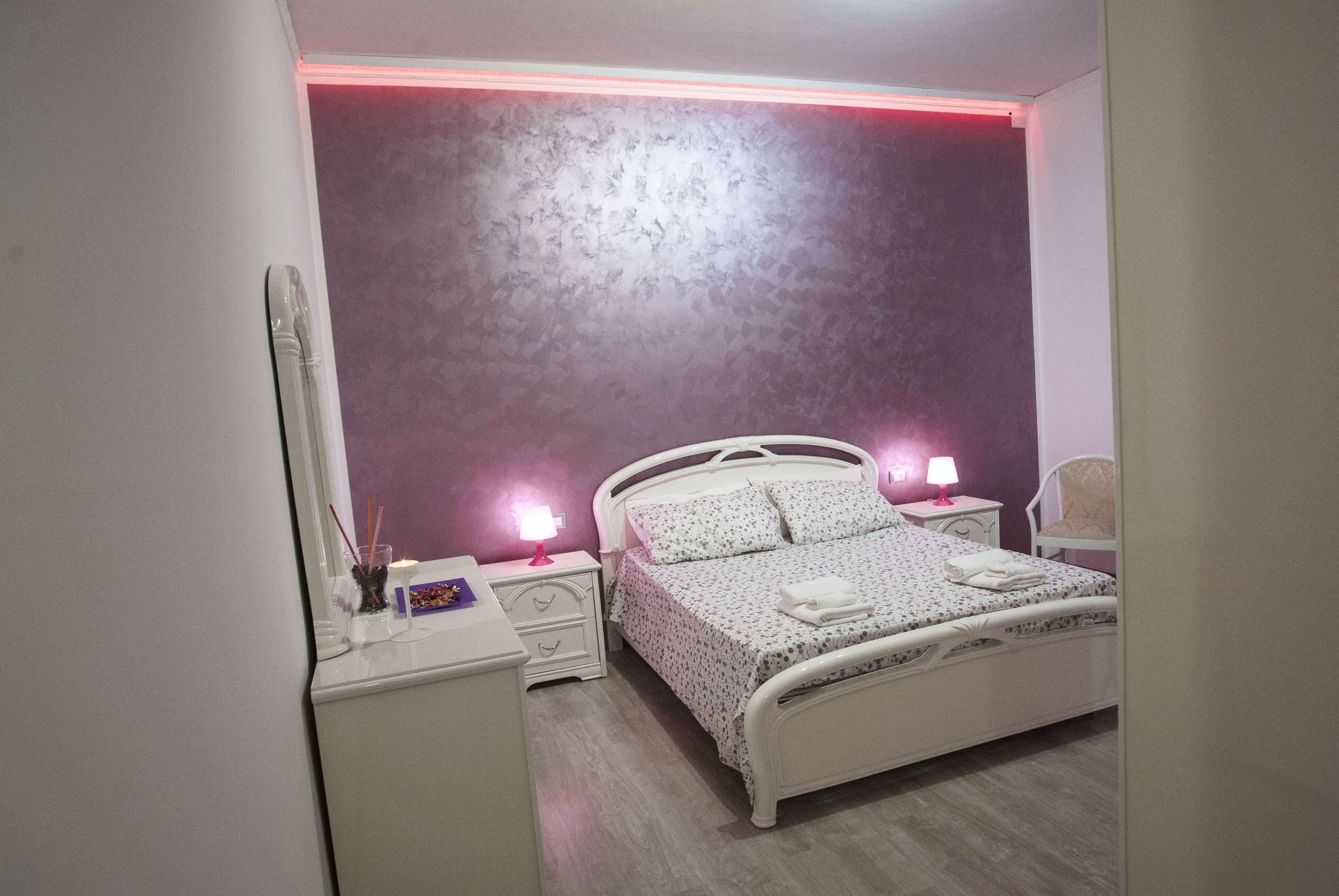 A bedroom with a white bed, two bedside tables with lamps, a mirror, and a chair.