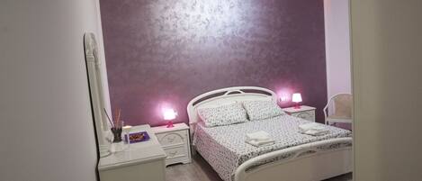 A bedroom with a white bed, two bedside tables with lamps, a mirror, and a chair.