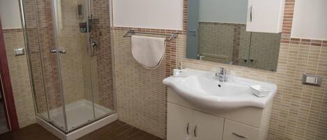 Un baño con ducha envuelta en vidrio, un lavamanos blanco y un espejo sobre él.