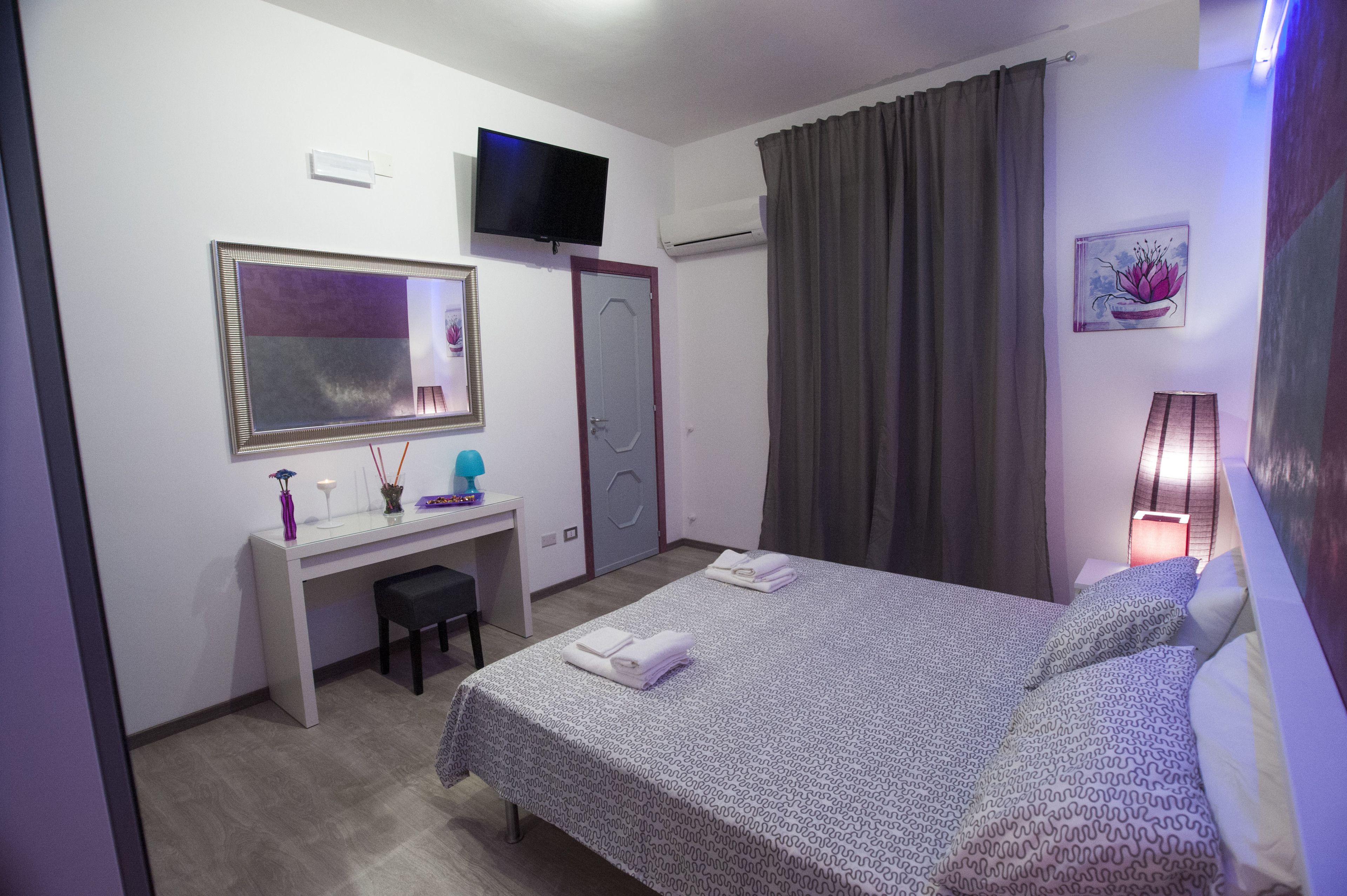 Ein Hotelzimmer mit Bett, Schreibtisch, Stuhl, Fernseher, Klimaanlage und einem Vorhangfenster.