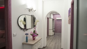 A narrow hallway with a wooden floor, a white wall, and a mirror above a vanity with a vase of flowers. - B&B Del Centro (Partinico)