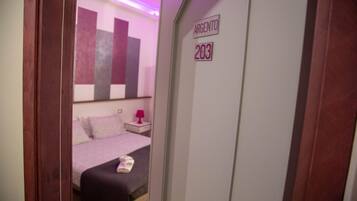 A hotel room with a bed, a nightstand, and a door labeled "ARGENTO 203".