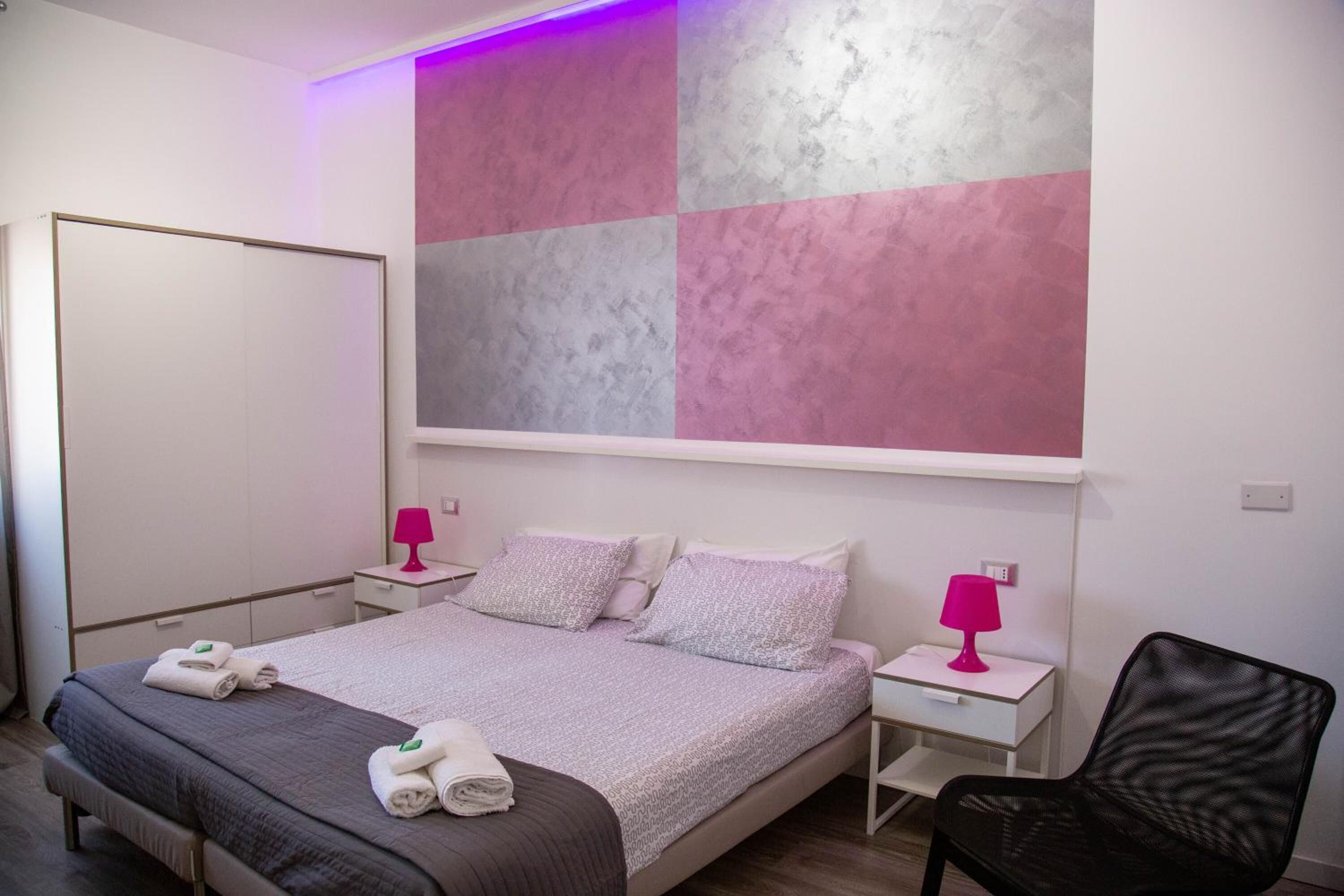 A bedroom with a bed, two bedside tables, a chair, and a large wall art piece.