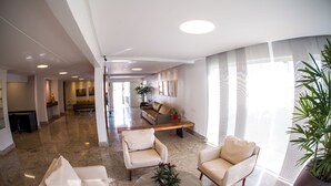 A spacious lobby with a modern design, featuring a seating area with sofas and armchairs, a coffee table, and a large potted plant. - Mundial Parque Hotel (Vicosa)