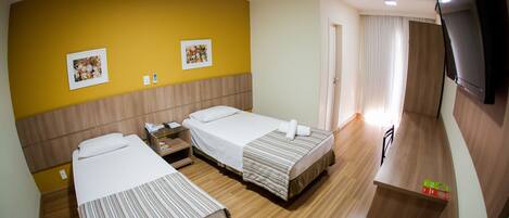 A hotel room with two beds, wooden flooring, a TV, and artwork on the walls.