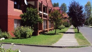 Um edifício de tijolos vermelhos com varanda, cercado por vegetação e um passeio.