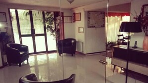 Uma sala de estar espaçosa com uma janela grande, uma poltrona preta, um sofá e uma escrivaninha com abajur.