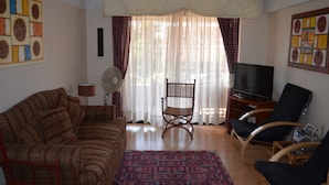 Uma sala de estar com sofá, duas poltronas, televisão e ventilador.