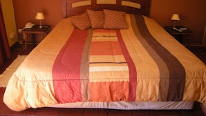 Uma cama com colcha listrada, duas mesas de cabeceira com abajures, e um quadro na parede.