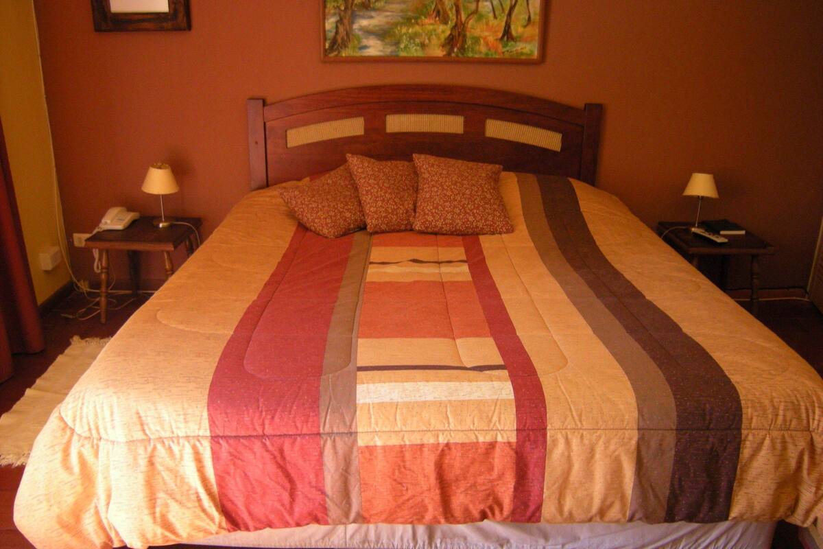 A bed with a striped bedspread, two bedside tables with lamps, and a painting on the wall.