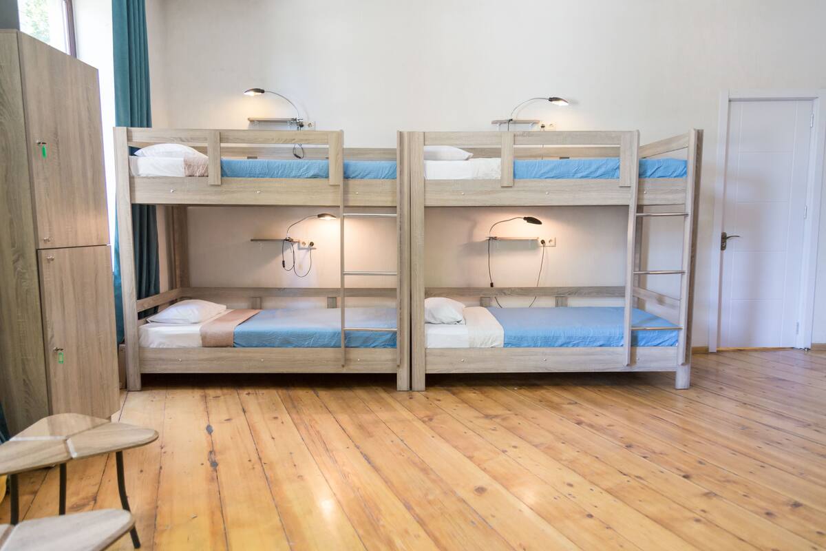 A bunk bed room with wooden floors, a wardrobe, and bedside lamps.