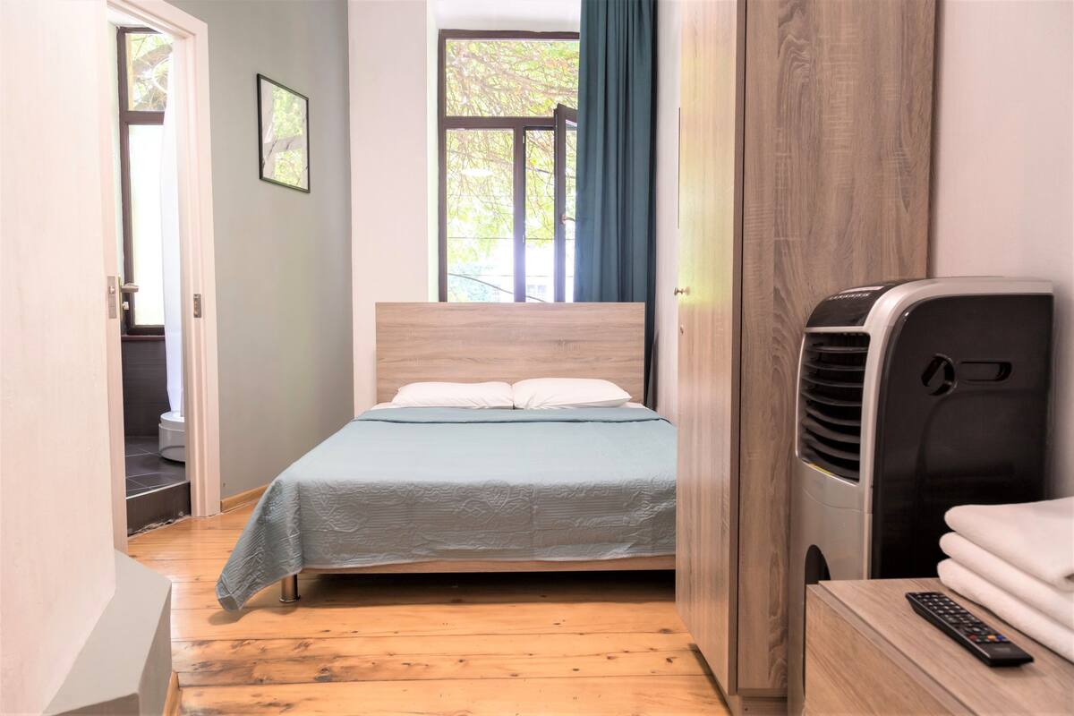 A bedroom with a bed, a wooden desk, a heater, and a window with curtains.