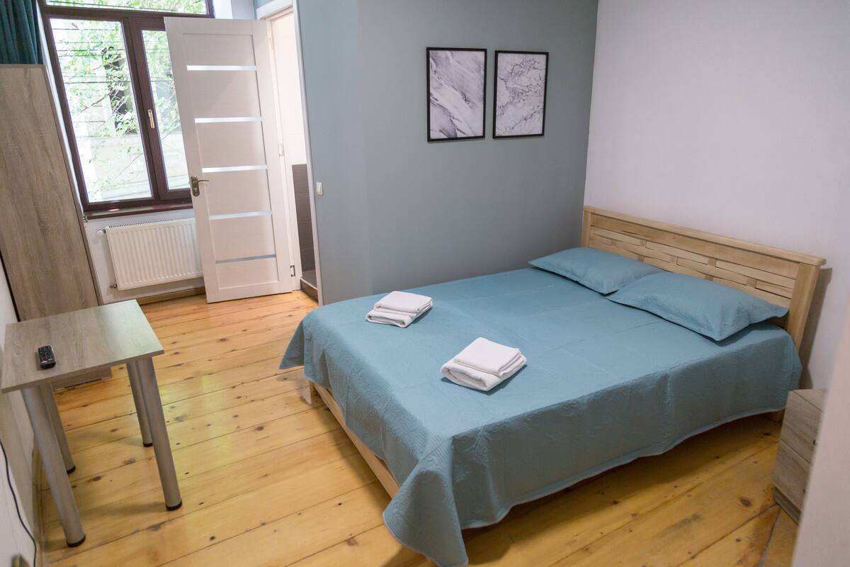 A bedroom with a bed, a table, and a radiator.