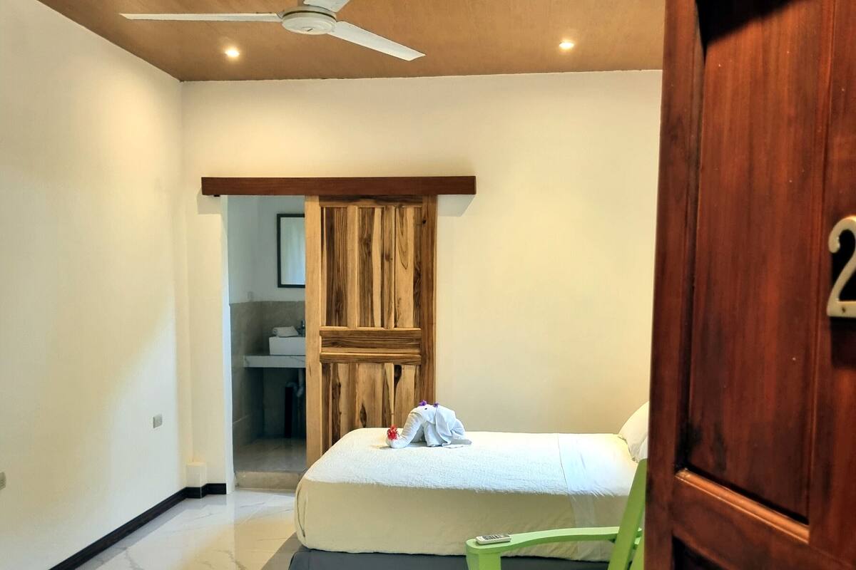 Une chambre à coucher avec un lit, une chaise verte, une porte en bois et un ventilateur de plafond.