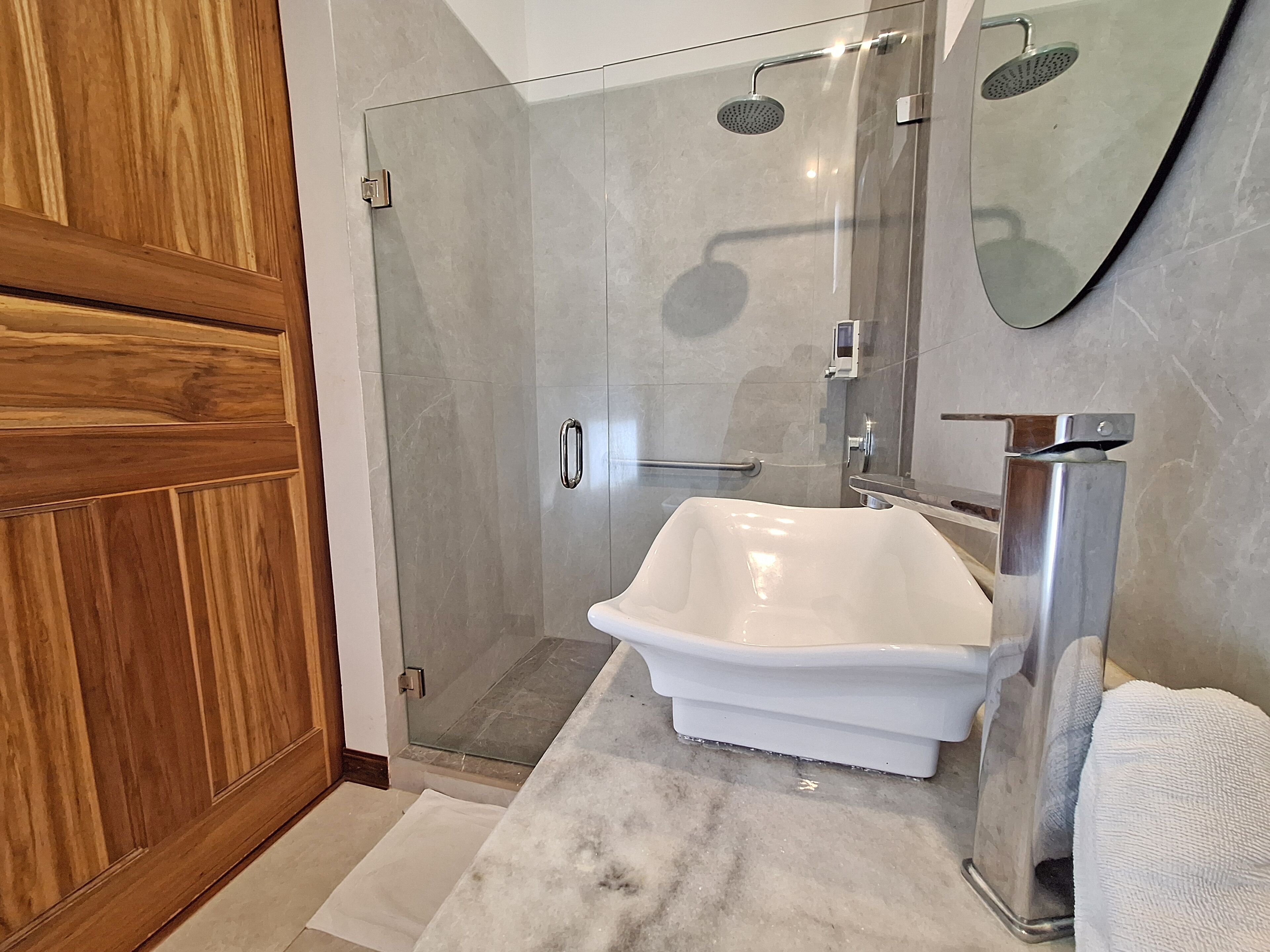 Une salle de bain avec une douche à parois de verre, un lavabo sur pied blanc et une porte en bois.