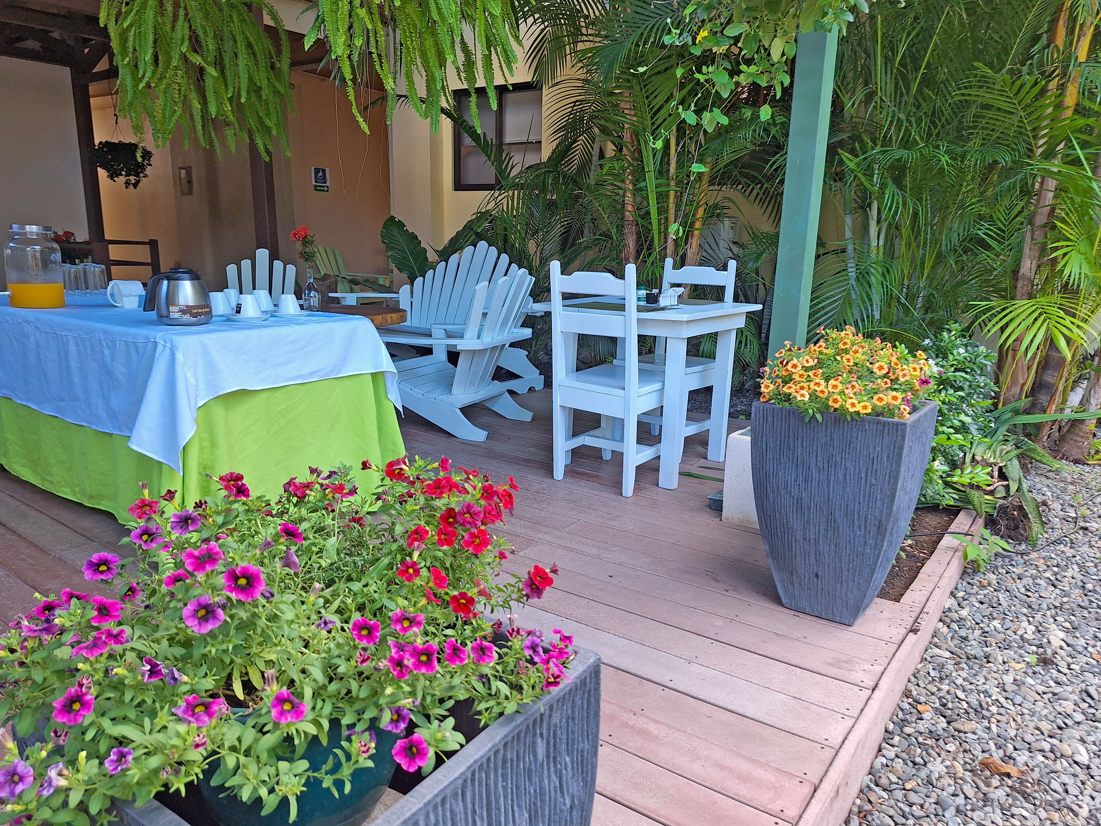 An outdoor seating area with a table set for two, surrounded by potted plants and chairs.