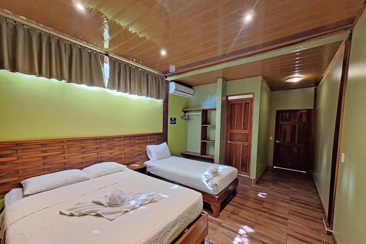 Une chambre d’hôtel avec deux lits, une tête de lit en bois, des murs verts et un plancher en bois.