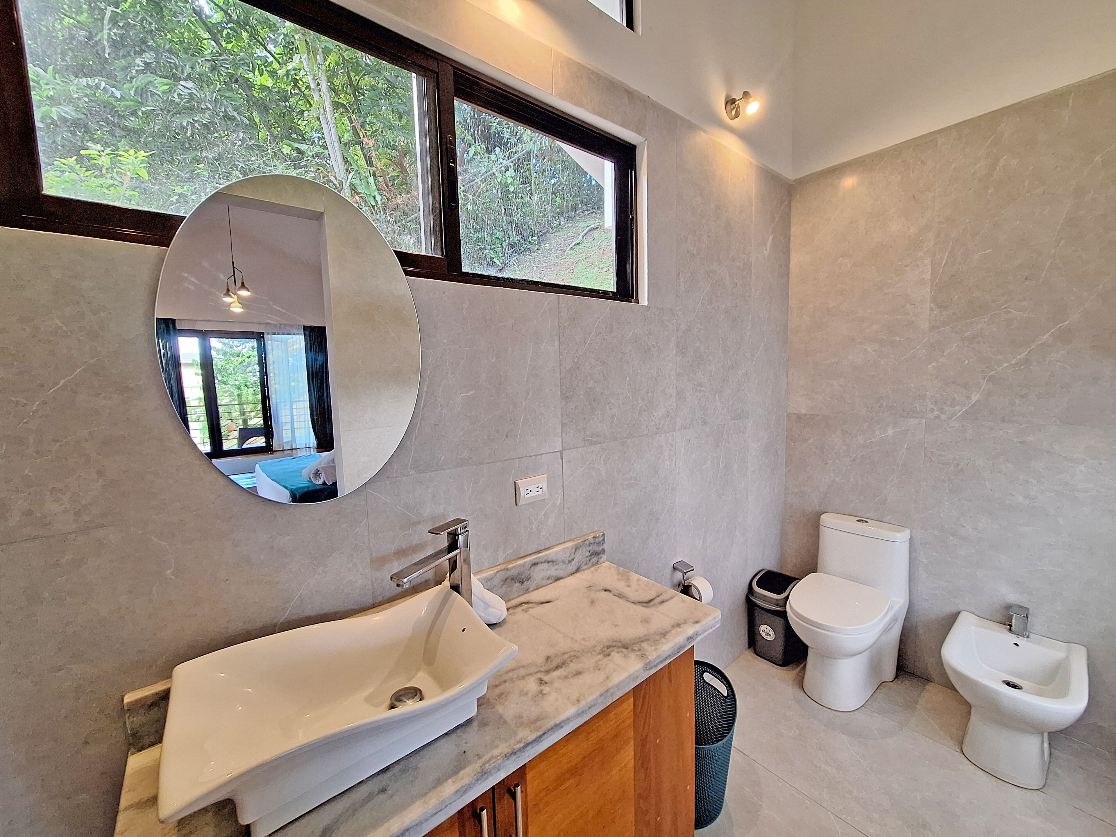 A modern bathroom with a large sink, mirror, and two toilets.
