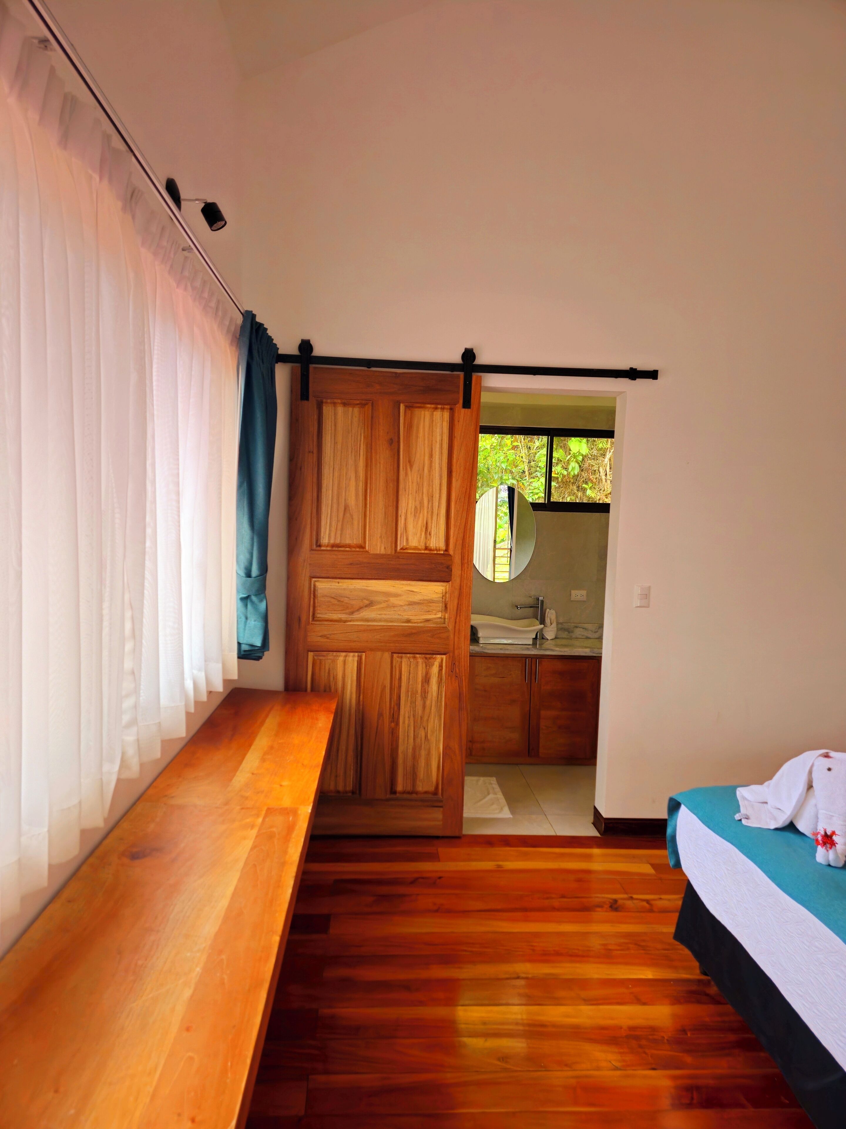 A bedroom with a wooden bed, a bench, a sliding door, and a view of a bathroom.