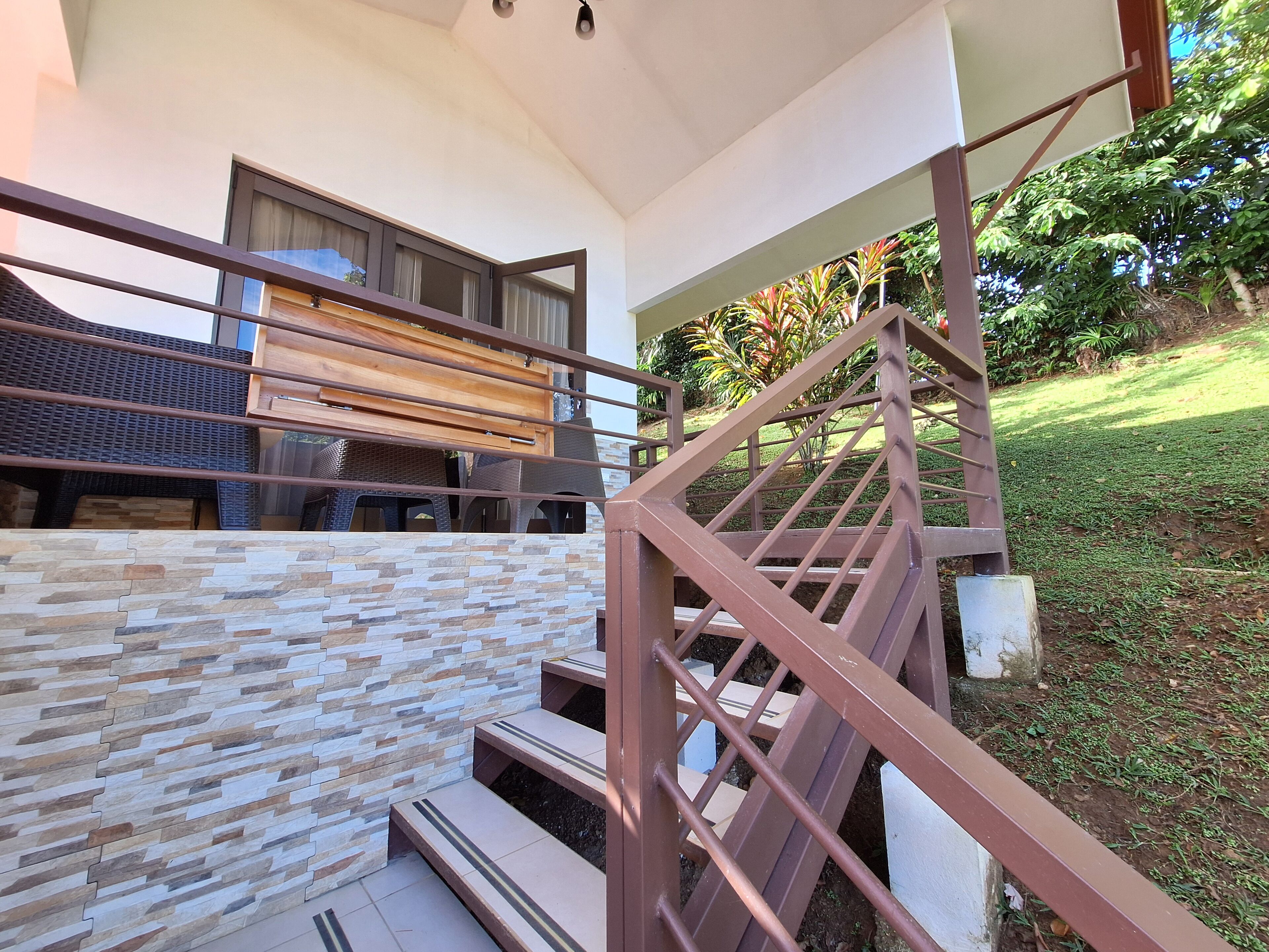 Una escalera moderna con pared de piedra y barandillas de metal que conduce a una terraza de madera.