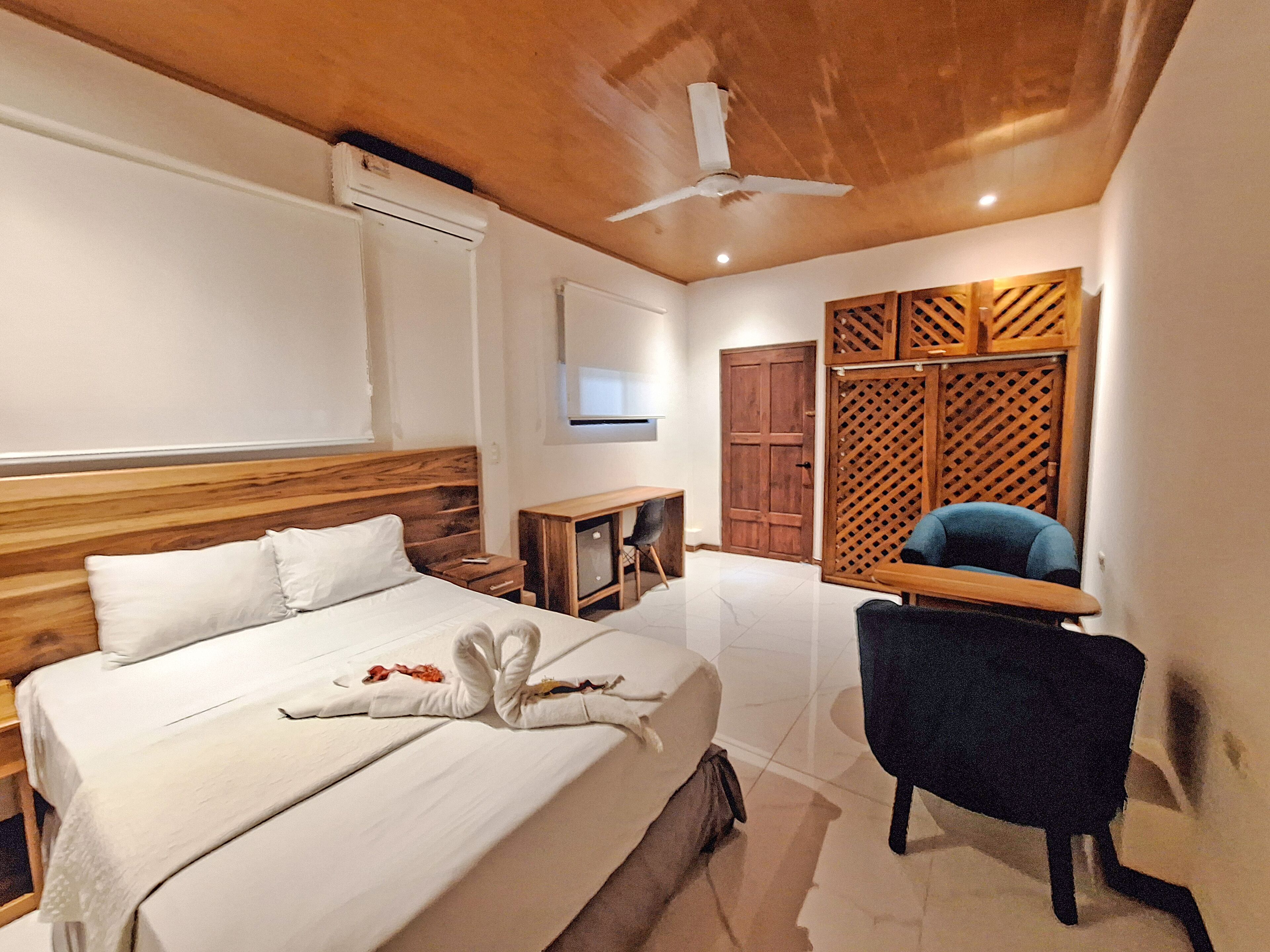 Ein Hotelzimmer mit hölzernem Kopfteil, einem Bett mit weißer Bettwäsche, einem Schreibtisch mit Stuhl, einem Fernseher und einem Holzschrank.