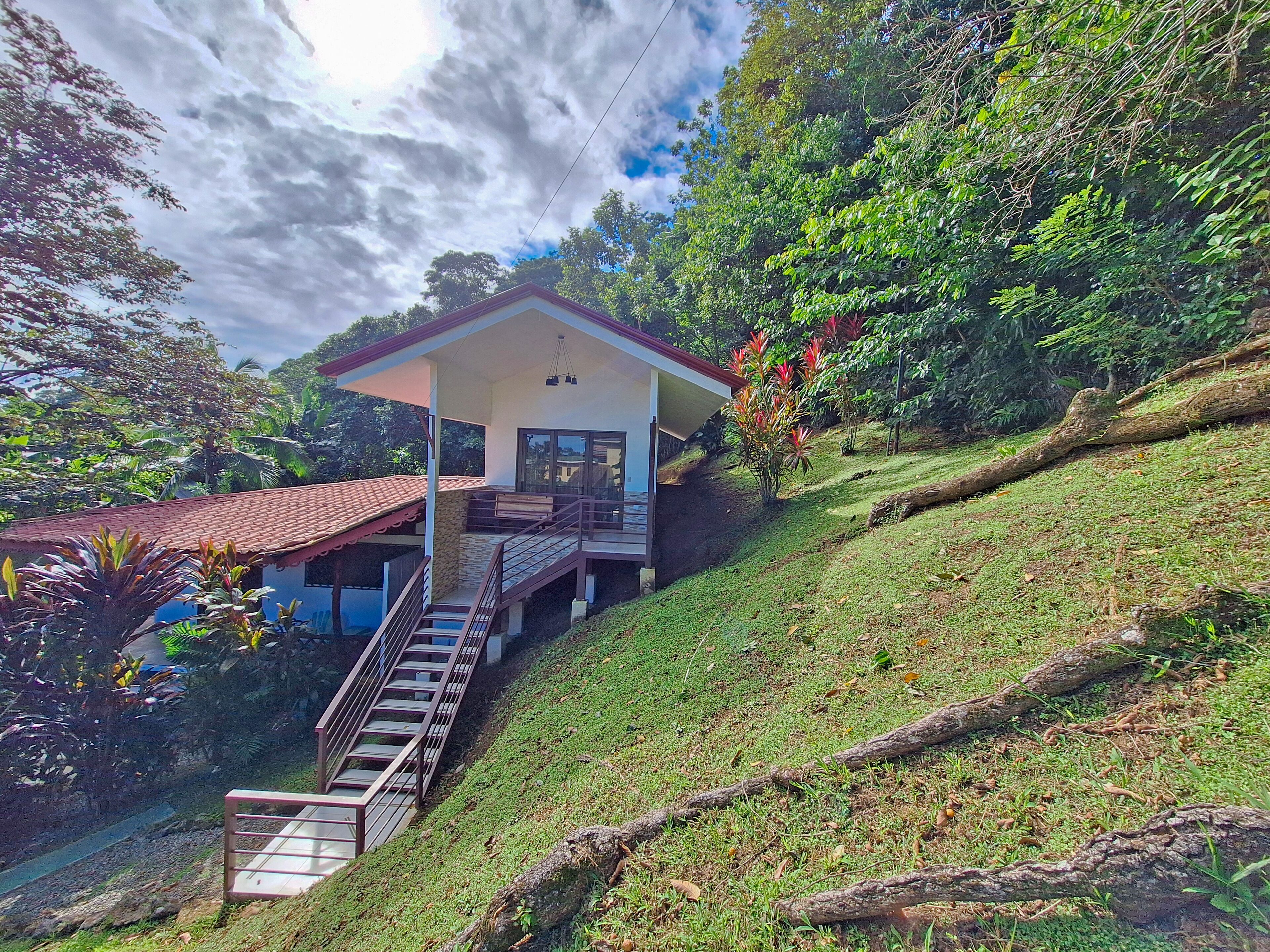 A house with a red-tiled roof, a balcony, and a staircase leading up to it.