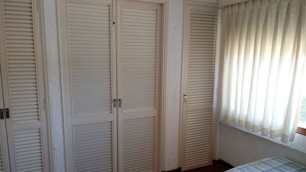 Ein Schlafzimmer mit einem Bett, einem Fenster mit Vorhängen und drei geschlossenen Türen.