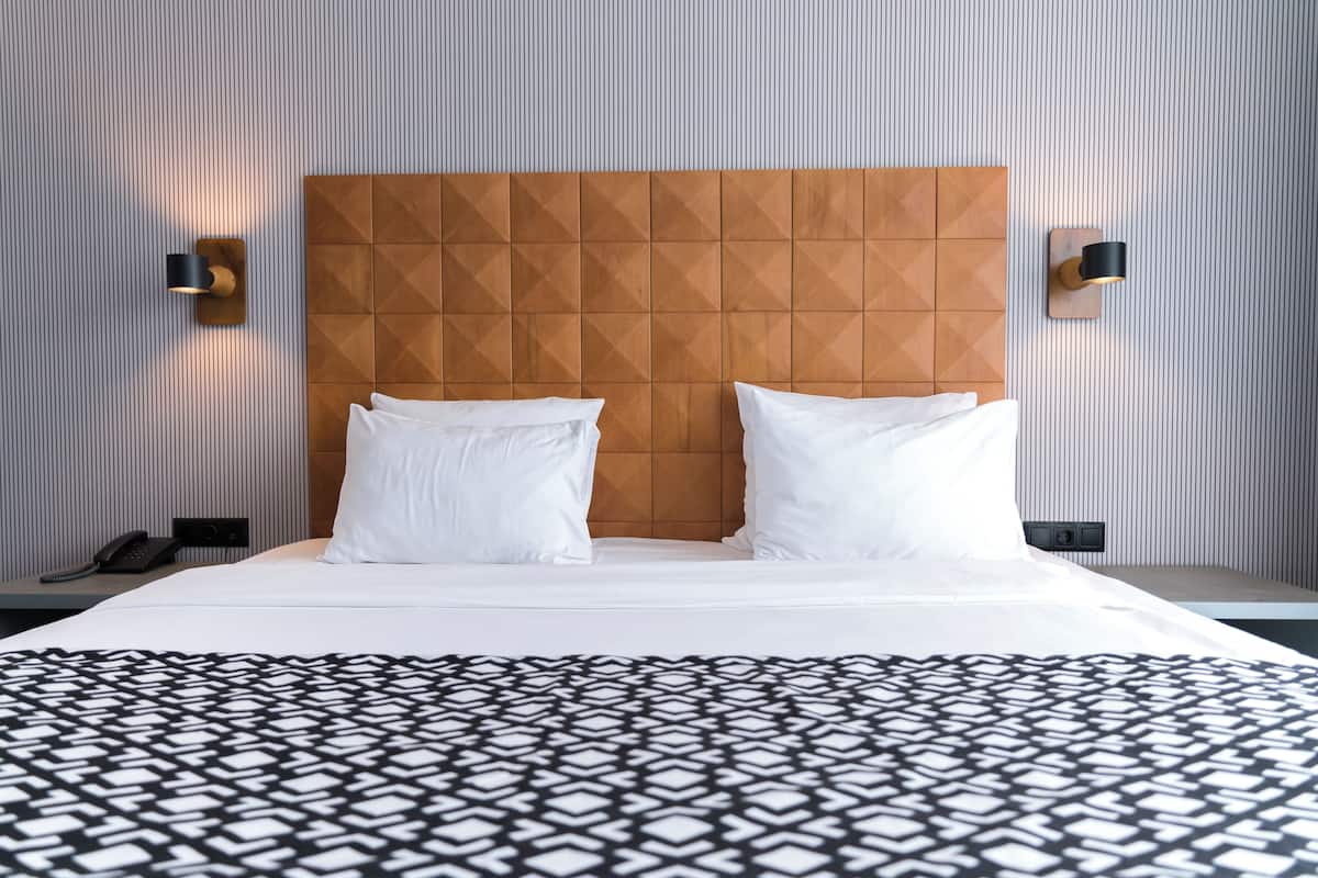 A hotel room with a large bed, two bedside tables, a wooden headboard, and two wall-mounted lamps.