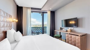 A hotel room with a large bed, a desk, a flat-screen TV, and a balcony with a view.