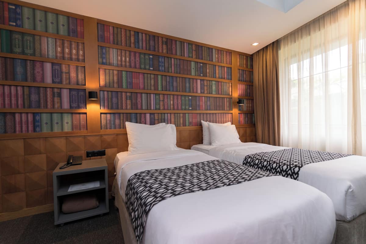 A hotel room with two beds, a bookshelf, and a nightstand.