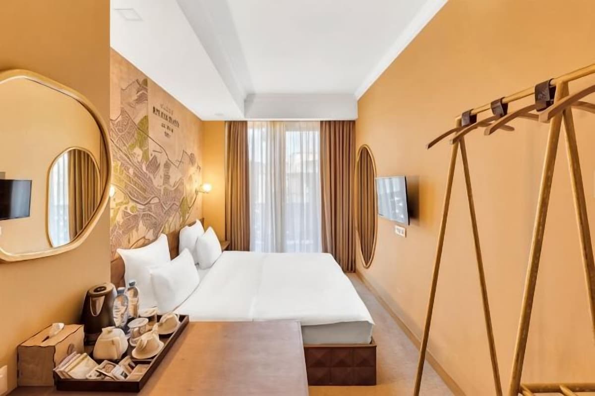 A hotel room with a large bed, a flat-screen TV, a map on the wall, and a wooden side table with a tray of items.