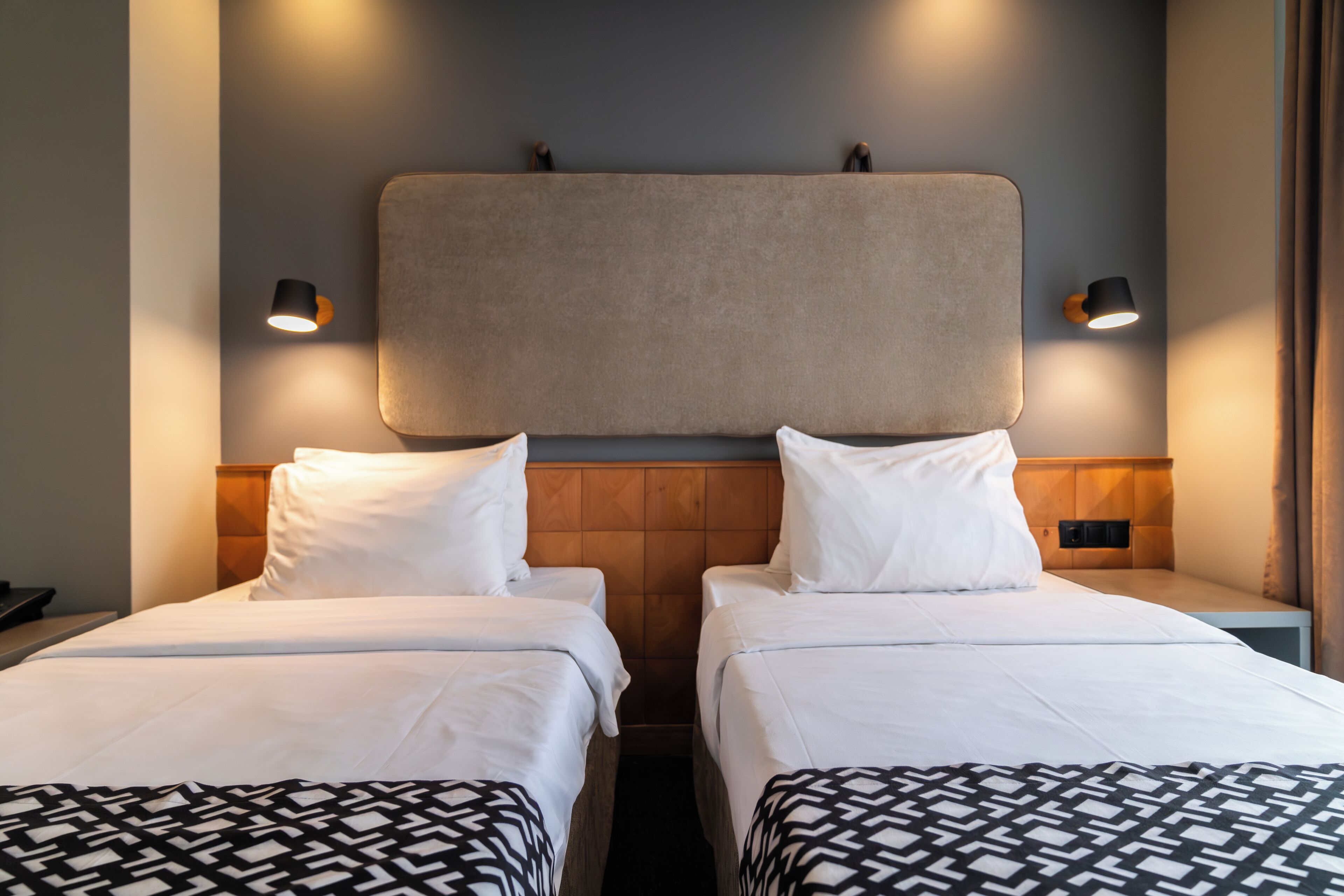 Ett hotellrum med två separata sängar, en sänggavel i trä och väggmonterade lampor.