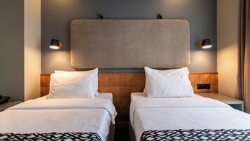 Ett hotellrum med två separata sängar, en sänggavel i trä och väggmonterade lampor.