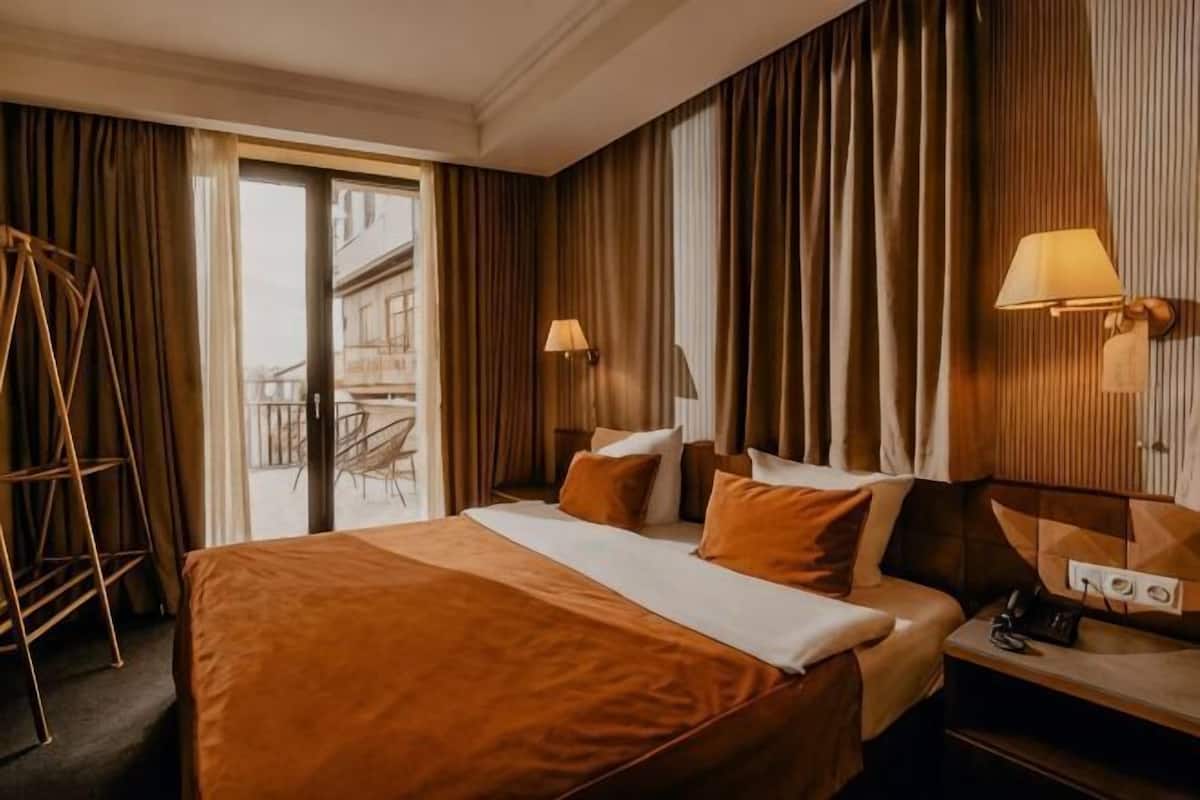 A hotel room with a large bed, two bedside lamps, a desk with a phone, and a view of the outside.