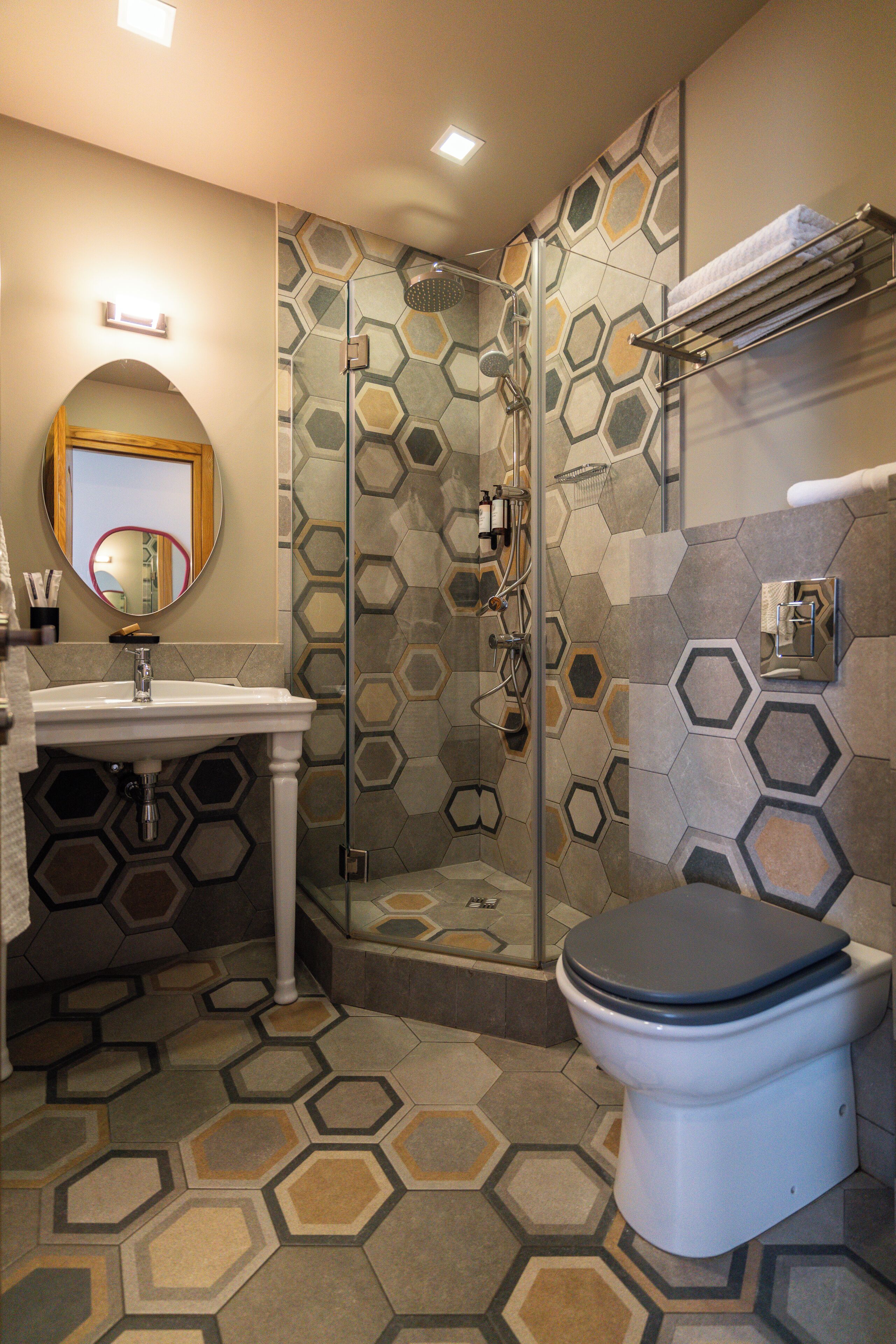 A bathroom with a hexagonal tile floor, a toilet, a sink, and a shower with a glass door.