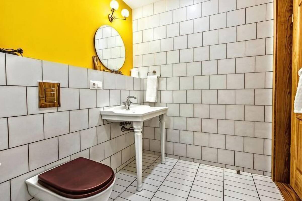 A bathroom with white tiles, a yellow wall, a white sink, and a wooden door.