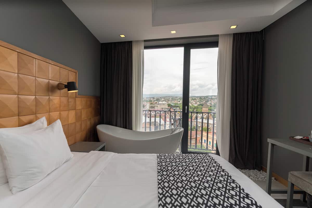 A hotel room with a large bed, a bathtub, a desk, and a view of the city.