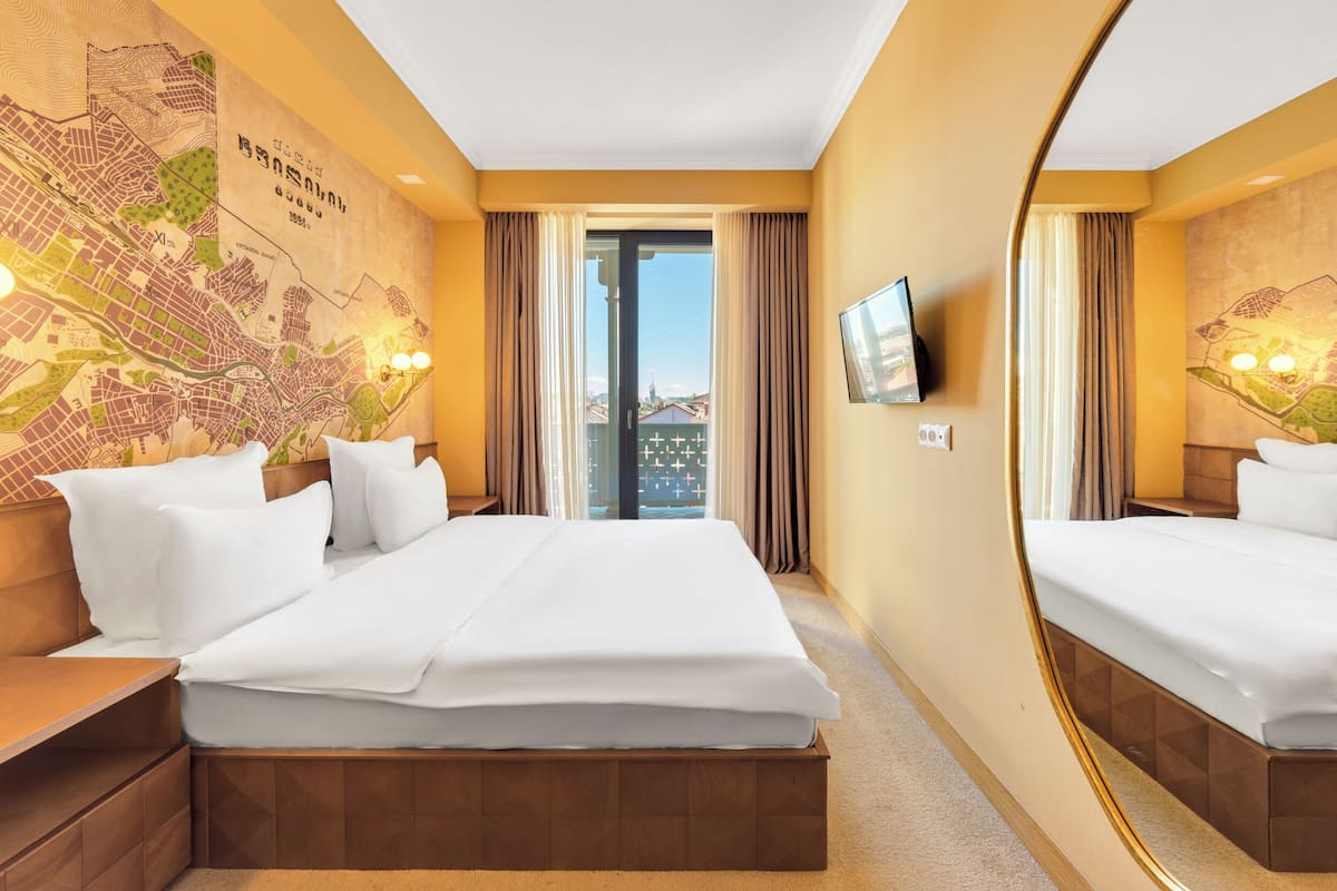 A hotel room with a large bed, a map on the wall, a TV, and a balcony with curtains.
