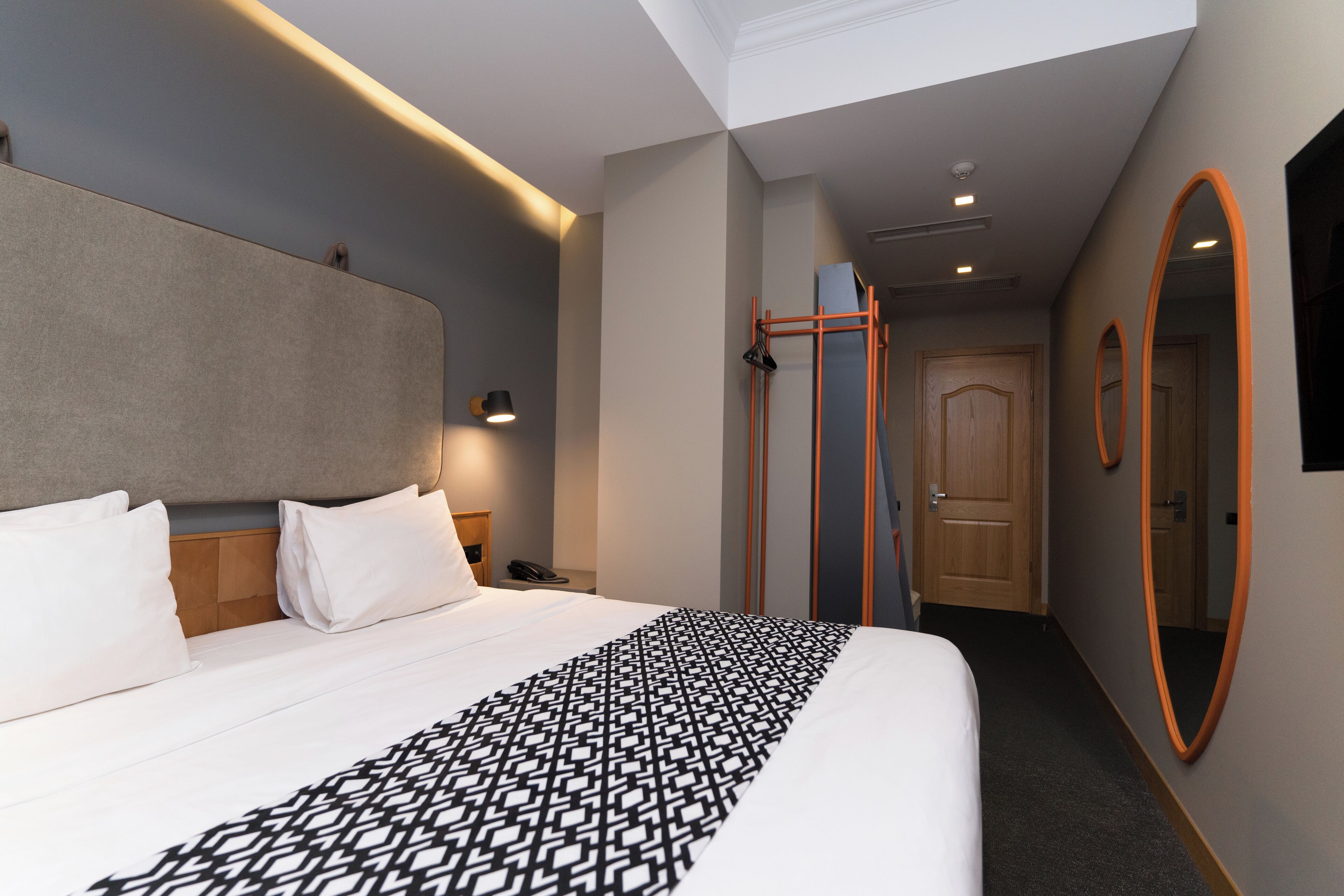 Une chambre d’hôtel moderne avec un grand lit, une tête de lit, une table de chevet, un téléphone et un miroir.