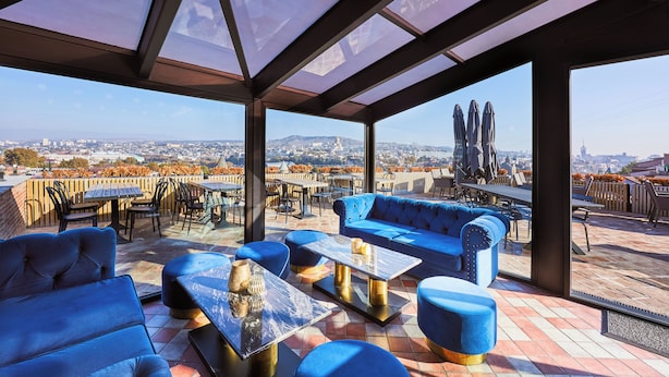 An outdoor seating area with blue furniture, a glass table, and a view of the cityscape.