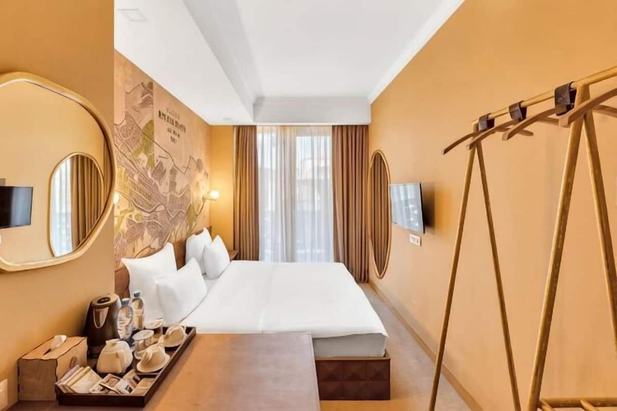A hotel room with a large bed, a flat-screen TV, a map on the wall, and a wooden side table with a tray of items.