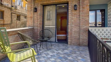 Un balcón con piso a cuadros, una silla y una puerta que da a una habitación.