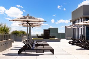 A rooftop terrace with outdoor seating, umbrellas, and a modern building in the background.