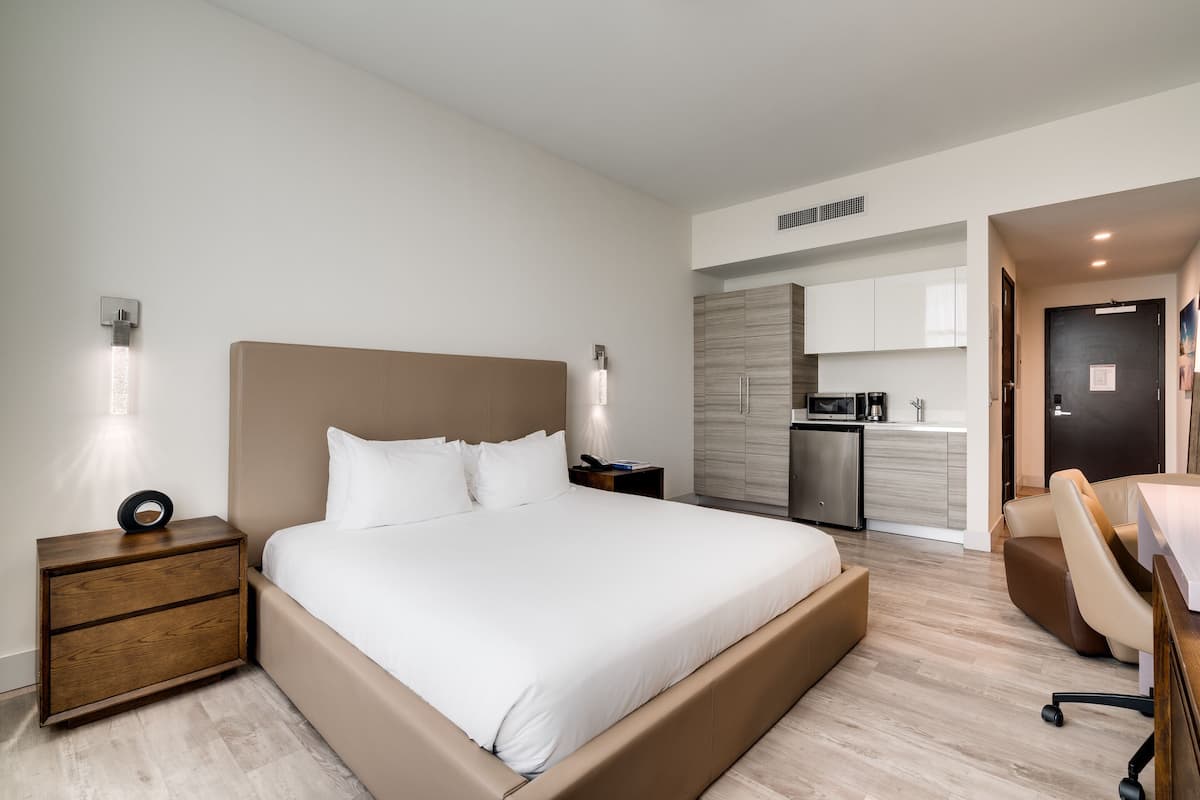 Une chambre d’hôtel moderne dotée d’un grand lit, de tables de chevet, d’un bureau et d’une kitchenette.